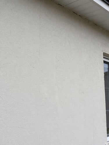 Detailed view of foundation parging application on residential exterior wall, uniform textured surface, trowel marks visible mid-work, natural overcast daylight, no people