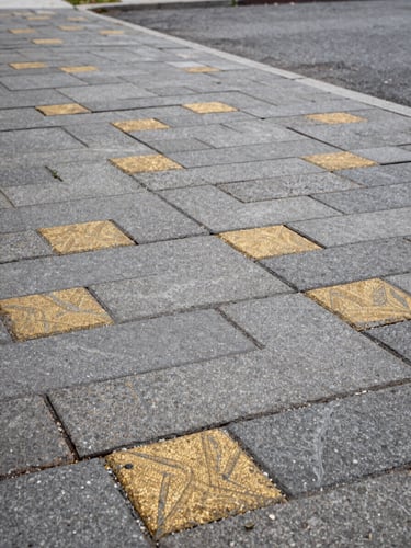 Close-up wide shot of freshly laid interlocking stone paving on a Montreal residential driveway, overcast daylight revealing precise joint lines and rich grey-gold stone texture, camera low and angled to show the material surface stretching to the left edge