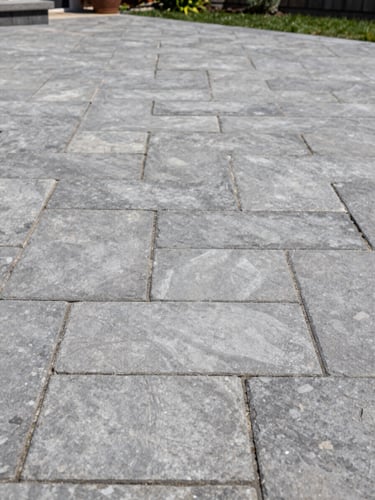 Detailed shot of premium interlocking stone patio installation, uniform joint lines and tight stone-to-stone contact, residential Montreal backyard, natural daylight from above, no people