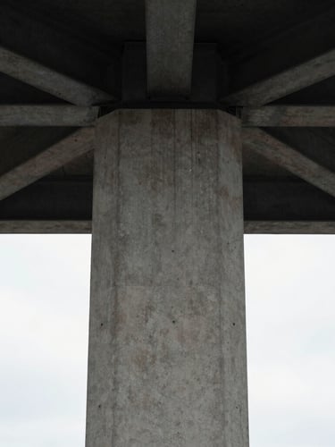 Symmetrical vertical crop of a modern concrete column meeting a dark steel ceiling beam, natural overcast light