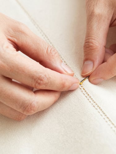 Close-up macro shot of a craftsman's hands hand-stitching a heavy canvas seam, natural high-key daylight, clean workshop setting.