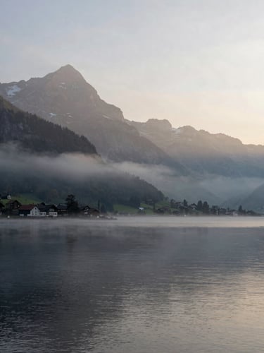 Quiet atmospheric landscape of the Lake Thun region in Switzerland at dawn, soft mountain silhouettes in morning mist, diffused natural light, panoramic 21:9 framing with generous negative space on the right.