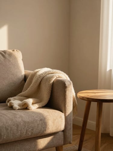 A softly lit corner of a warm farewell room with a comfortable armchair, natural wooden side table, soft wool blankets, and diffused warm indoor light.