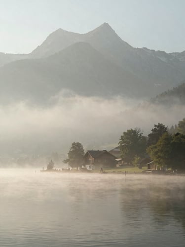 A calm, misty morning landscape of Lake Thun, soft silhouettes of the Bernese Alps in the background, diffused natural light, peaceful and quiet atmosphere.