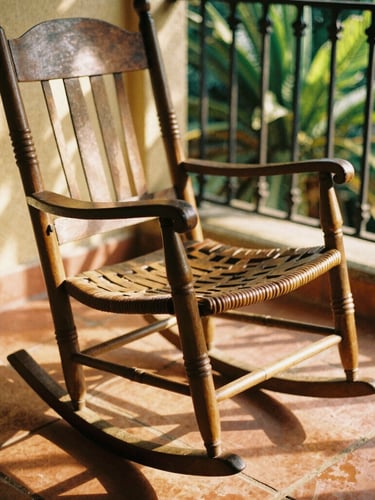 Close-up of a traditional rocking chair on terracotta tiles, warm golden-hour light filtering through colonial iron grilles, soft shadows, 35mm film style