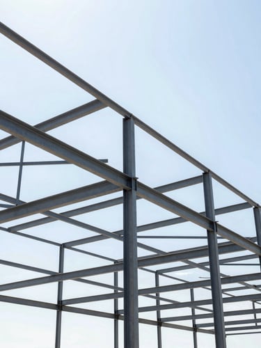 Low-angle architectural photography of a heavy steel warehouse frame under construction, bright direct Florida daylight, high-contrast iron gray steel beams against a clear sky