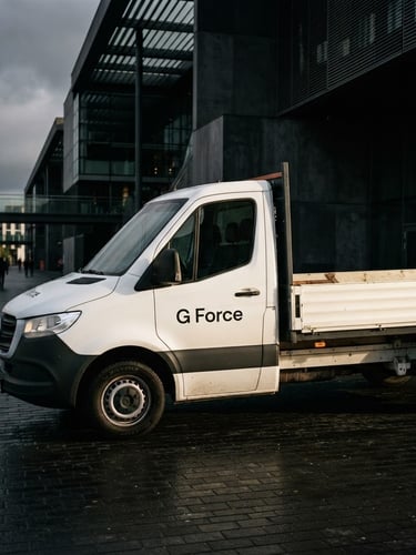 A clean white drop-side delivery van with minimalist black 'G Force' branding parked outside a modern architectural building, moody editorial photography, high-contrast side lighting, 35mm.