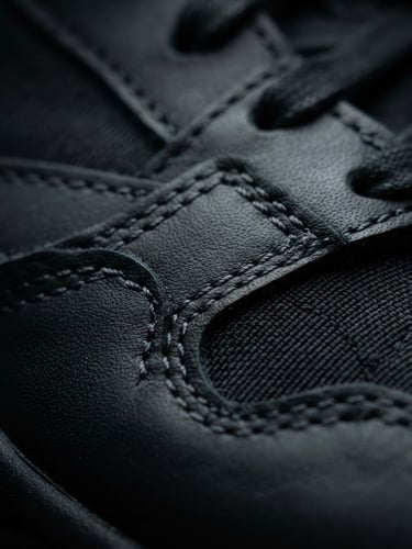 Extreme close-up of a luxury sneaker stitching, dramatic studio rim lighting, deep black and charcoal tones, sharp focus, 85mm lens