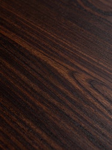 Extreme close-up of dark mahogany wood grain with deep natural shadows, reflecting low side-light, showcasing rich organic textures.