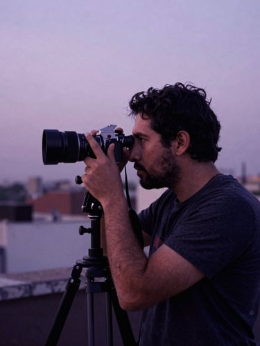 Cinematic 35mm film photography of a film director looking through a viewfinder on a CDMX rooftop at dusk, deep plum shadows, soft overcast lavender sky.