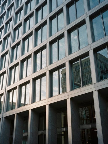 Wide architectural shot of a modern corporate building facade reflecting cool morning light, clean lines, minimalist geometry, high contrast.