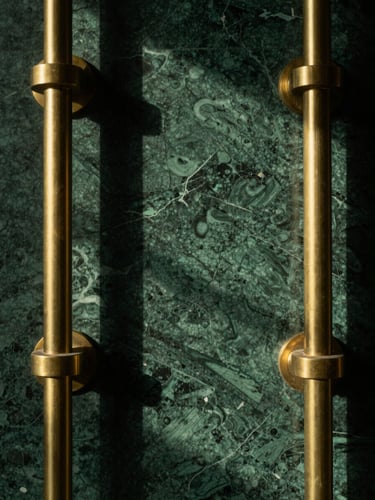 Macro photography of brushed brass fixtures against deep emerald green marble, warm directional lighting casting soft shadows, cinematic and highly detailed.