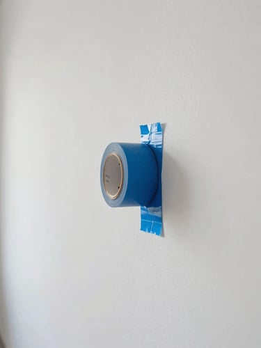 Straight-on architectural photograph of a clean, sharp paint line being revealed as blue painter's tape is slowly peeled back from a pristine gallery-white wall, natural side-light, high-end precision detail
