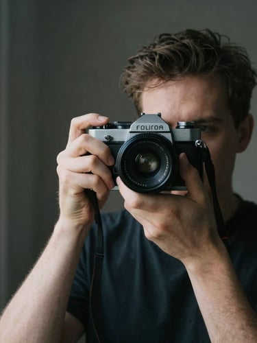 Intimate portrait of a photographer holding a classic rangefinder camera, natural side light from a window, soft film grain, dark minimalist background