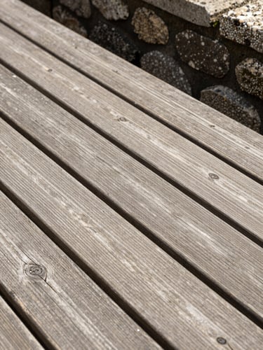 Vue rapprochée d'une terrasse en bois de qualité supérieure, les lames de bois s'ajustent parfaitement contre un muret en pierre de taille, lumière naturelle vive.