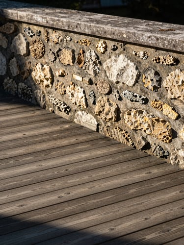 Vue rasante d'une terrasse en bois de qualité supérieure et d'un muret en pierre de taille propre, baignés par une lumière naturelle du matin à Nancy, cadrage professionnel.