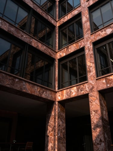 Low-angle architectural photograph of an elegant modern stone and glass office building in Tulancingo, dramatic high-contrast lighting, deep shadows, rich copper tones, 35mm