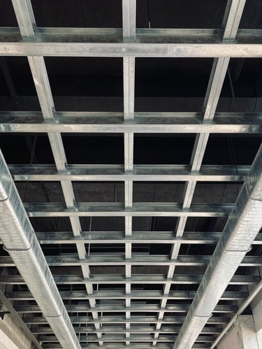 High-contrast architectural view looking directly up at a perfectly aligned ceiling grid of exposed stainless steel ductwork and conduit runs, cool ambient daylight.
