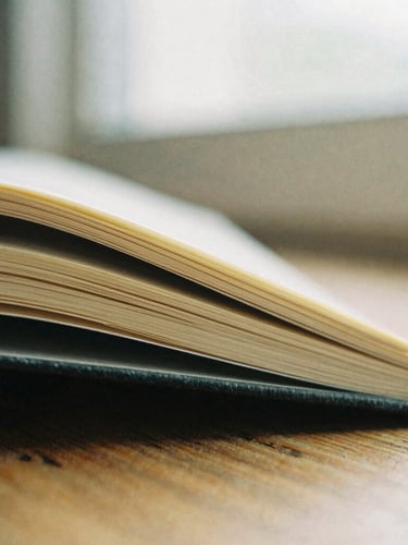 Macro close-up of deckled-edge book pages resting on a rustic wooden surface under soft, diffused overcast window light, warm paper tones, shallow depth of field, editorial 35mm film style