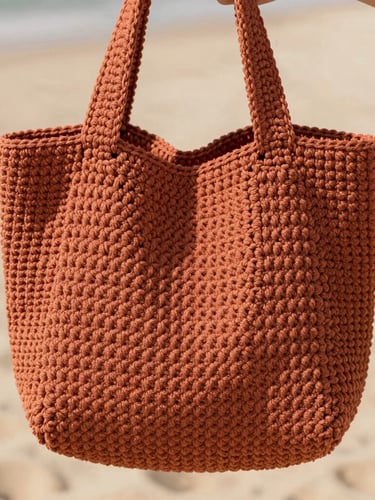 A close-up of a structured minimalist crochet bag in terracotta color, held by hands, soft natural daylight, warm sand background, macro texture detail, shallow depth of field, 35mm