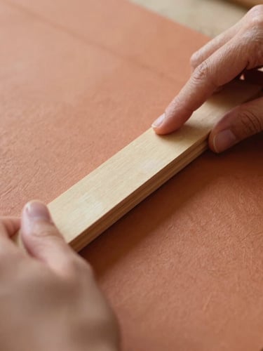 Warm editorial photography, close up of hands folding thick textured terracotta paper with a bone folder, soft natural afternoon light, shallow depth of field, 35mm