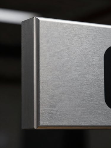 Extreme close-up of a fabricated aluminum sign edge under flat studio lighting, crisp beveled corner and brushed metal surface texture visible in sharp detail, dark background