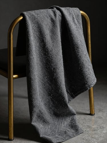 Close-up of textured charcoal fabric draped over a modern brass chair, dramatic interior lighting with deep shadows.