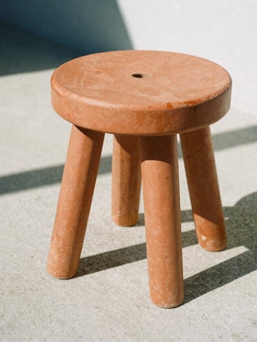 Low-angle architectural close-up of a heavy terracotta resin stool on a raw concrete patio, harsh midday sun casting sharp geometric shadows, medium format film.