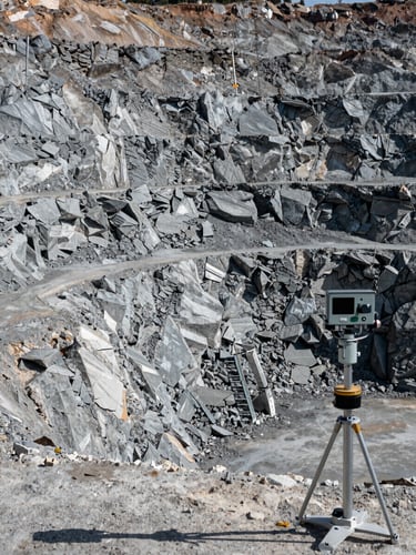 Wide panoramic view of a large open-pit mine slope face, exposed rock strata and geological layers visible in sharp daylight, measuring stakes and inclinometer instruments in the foreground right, cool north-facing natural light revealing precise texture of fractured rock, no people, no equipment in operation