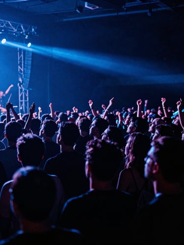 A dramatic wide-angle shot of a live concert crowd under intense blue stage lights, heavy shadows, raw energy, high-contrast.