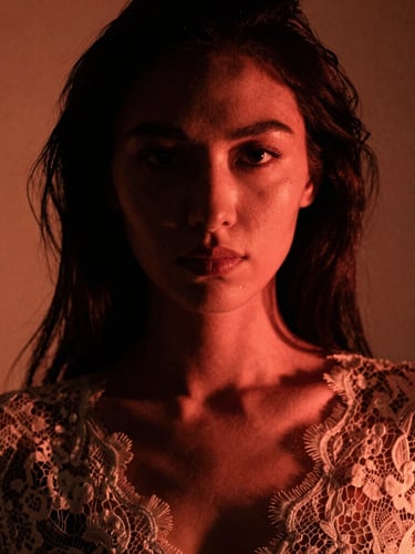 Close-up artistic portrait of a woman in elegant lace, dramatic low-key lighting with deep shadows and soft warm neon backlighting, high-contrast, fine 35mm film grain, editorial style.