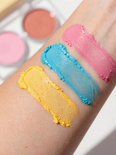 Vibrant close-up of colorful makeup swatches on warm skin tones under bright natural daylight, shallow depth of field