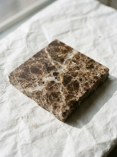 Luminous editorial photography, bright natural daylight, close-up of brown Emperador marble sample resting on a sheet of white Tyvek, soft shadows, high-contrast, 35mm