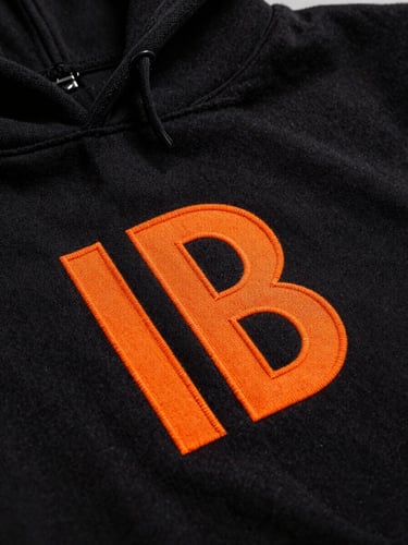 Extreme macro close-up of vibrant safety orange ink curing on a heavy black cotton hoodie, dramatic studio lighting with deep shadows, showcasing the rich texture of the fabric fibers and raised print details.