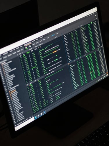 Close overhead crop of a deployment dashboard on a wide monitor, terminal logs scrolling on the left pane, uptime metrics and green status indicators on the right pane, cool fluorescent lighting reflecting on the screen surface, no people, dark desk environment