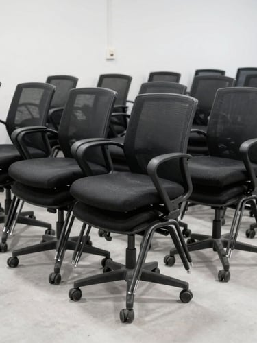 Wide environmental shot of organized rows of black office chairs stacked in a clean, brightly lit corporate floor post-removal, industrial editorial photography, 35mm lens