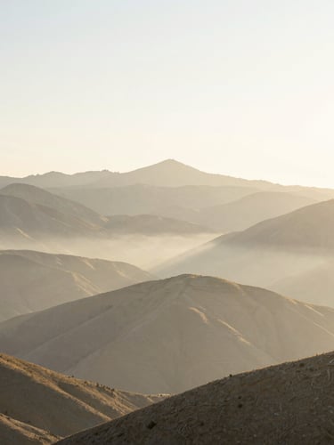 Expansive natural Utah mountain landscape at dawn, first morning light hitting the peaks, soft golden mist, wide environmental shot with generous negative space, airy high-key lighting