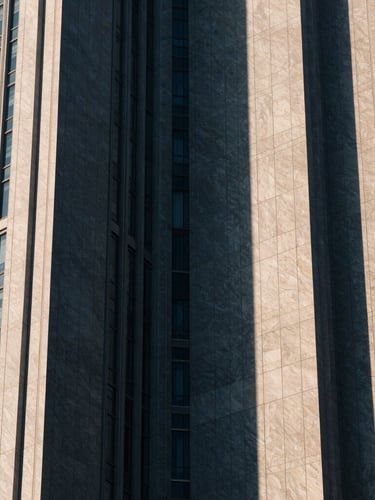 Abstract architectural crop of modern financial district skyscraper, sharp geometric shadows, muted navy and champagne tones, high-contrast, 35mm lens