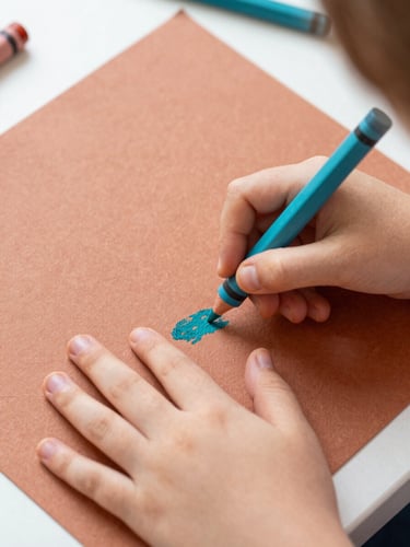 Overhead shot of a child's hands coloring a textured paper sheet with earthy terracotta and teal crayons, soft morning daylight, shallow depth of field
