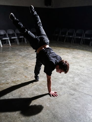 Ground-level framing of a freestyle dancer locked in a mid-freeze, one hand planted on a concrete floor, body suspended at an acute angle. Side-angle strobe lighting cuts hard shadows across the floor surface. The battle space is visible in the background — empty chairs, a dim venue, no crowd. Shot from torso height looking down toward the floor.