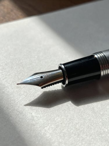 Close-up macro shot of a high-quality fountain pen resting on heavy textured cotton paper. Overcast natural light from a side window, dramatic architectural shadows.