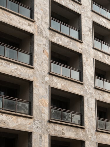 Close architectural detail of a completed residential building facade in Mumbai — precise stone cladding joints and aluminium window framing under north-facing daylight, accurate material color, no people, no text