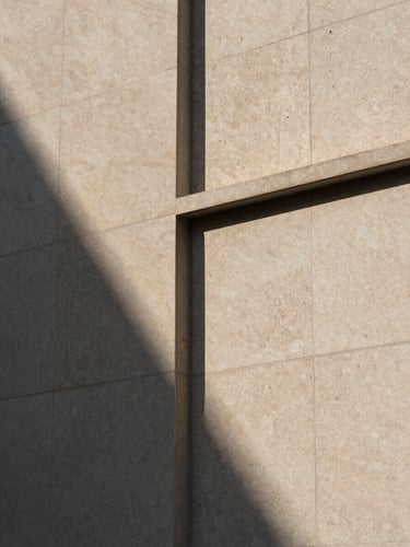 Close architectural detail of a completed building facade — precision-cut stone cladding panels meeting at a geometric shadow joint, natural daylight raking across the surface to reveal material texture and alignment, no people, neutral color grading