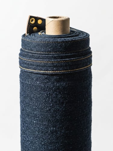 High-contrast studio fashion photography, sharp focus on a roll of premium raw denim fabric, golden hardware accents, minimalist white backdrop, 85mm
