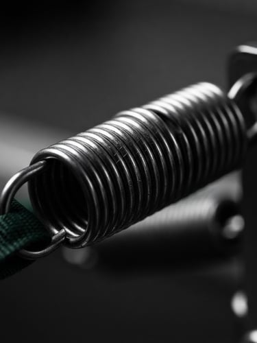 Macro close-up of high-tensile steel Pilates springs, clean minimalist studio lighting, high-contrast black and white with subtle green accents, 50mm