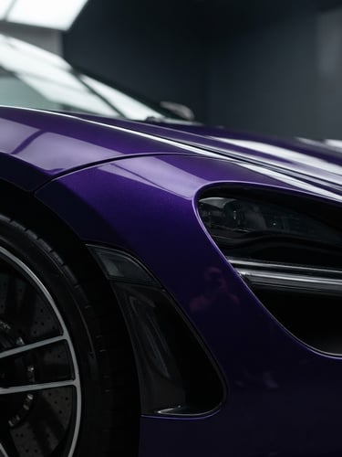 Sleek close-up of a luxury sports car fender with pristine deep purple metallic paint, soft studio light reflecting on curves, high-contrast specular highlights