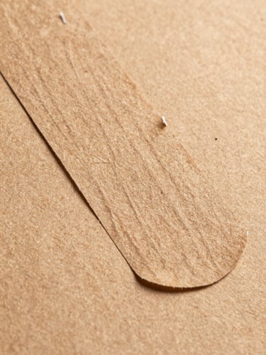 Extreme close-up of a kraft paper mailer adhesive strip being peeled, revealing the permanent seal layer, kraft weave texture sharp in foreground under flat north-facing studio overhead light, brown paper grain filling the frame edge-to-edge