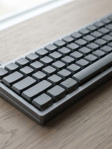 Close-up of a sleek physical aluminum keyboard on a warm gray wooden desk, soft diffused natural light, minimalist editorial photography, 35mm lens