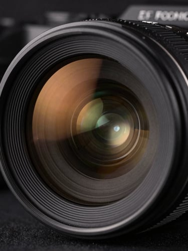 Sharp close-up of a high-end camera lens showing amber reflections on the glass element, dark industrial studio background, crisp focus, 50mm lens