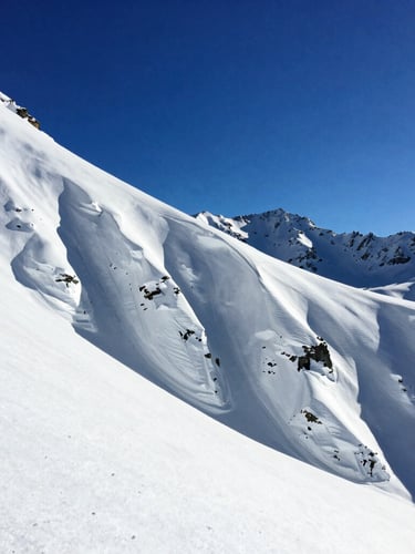 High-contrast alpine photography of steep vertical snow chutes in Las Leñas under crisp winter sun, deep blue sky, 35mm